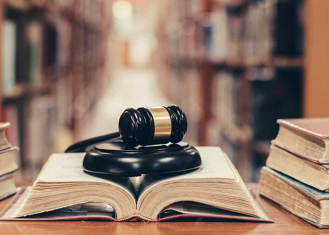 A photo of a gavel sitting on an open law book, the stacks of a library out of focus in the background.